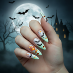 Hand with long stiletto nails in Batty Glow — milky white with black bat glitter and orange gems glowing in the dark against a Halloween night background