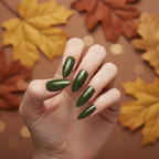 Hand with long stiletto nails in Golden Canopy — deep olive green with fine golden micro-glitter shimmer against an autumn background